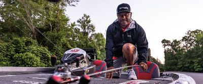 Pro angler Mark Daniels Jr. kneels down on a fishing boat looking at the camera while holding a fishing rod. 